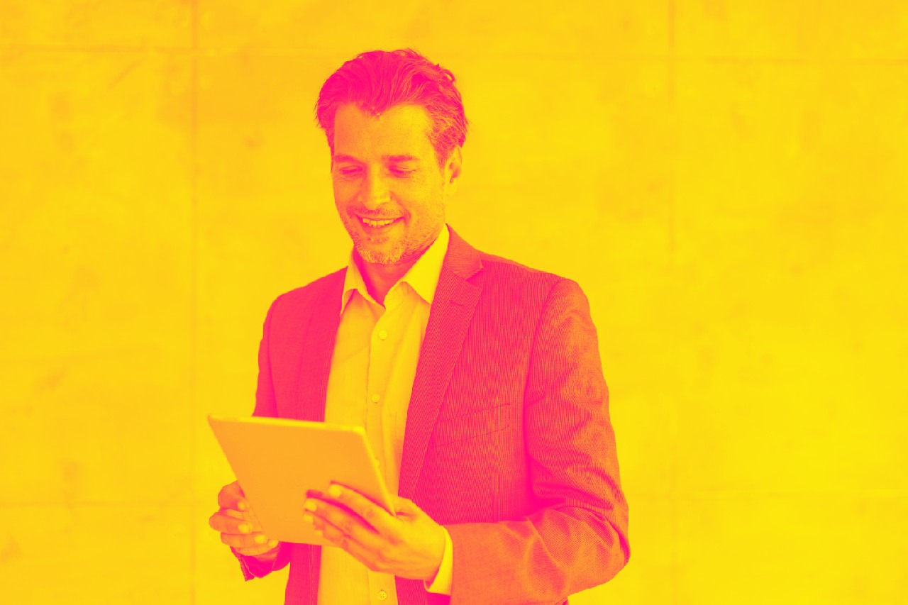 A businessman smiles and holds a tablet, after he discovered how to reduce costs with global ACH and real time payments